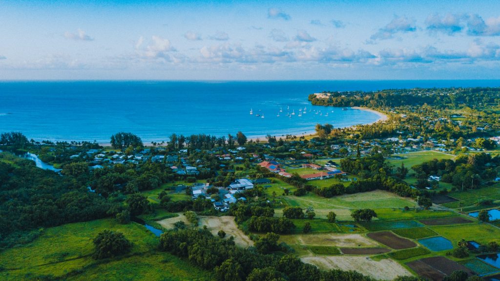 Aerial view of Hanalei Bay's crescent-shaped shoreline with sailboats and lush green fields.