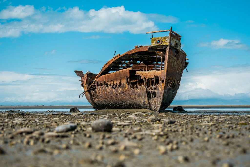 Rusty shipwreck stranded on a rocky shore under a blue sky.