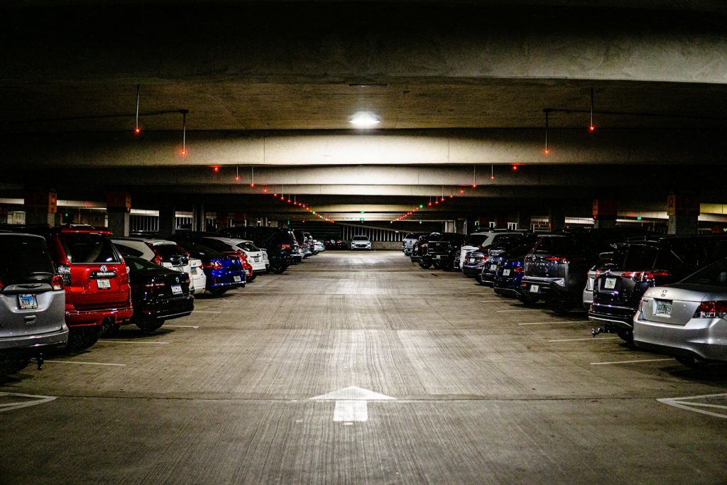 Multi-level parking garage with rows of cars and red availability indicators on the ceiling.
