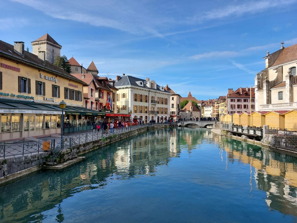 Canal in Annecy's old town with colorful buildings, restaurants and a medieval castle reflected in the water.