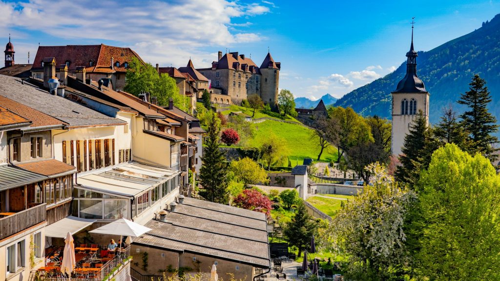 Medieval town of Gruyères with its 13th-century castle on a hilltop surrounded by green Alpine scenery.