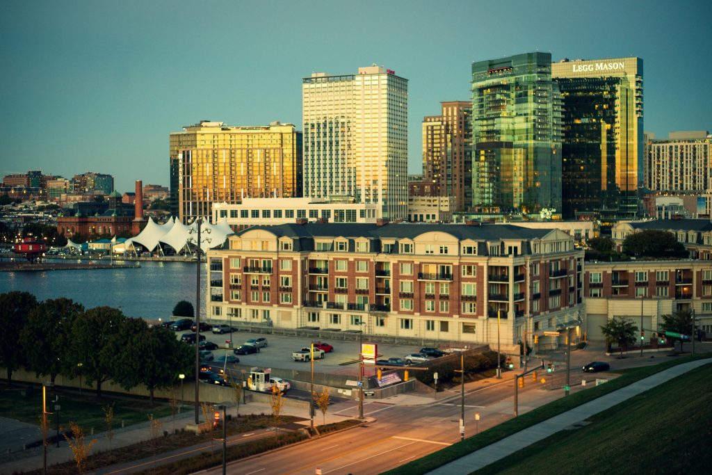 Baltimore's waterfront with residential buildings, harbor and illuminated downtown skyscrapers at dusk.