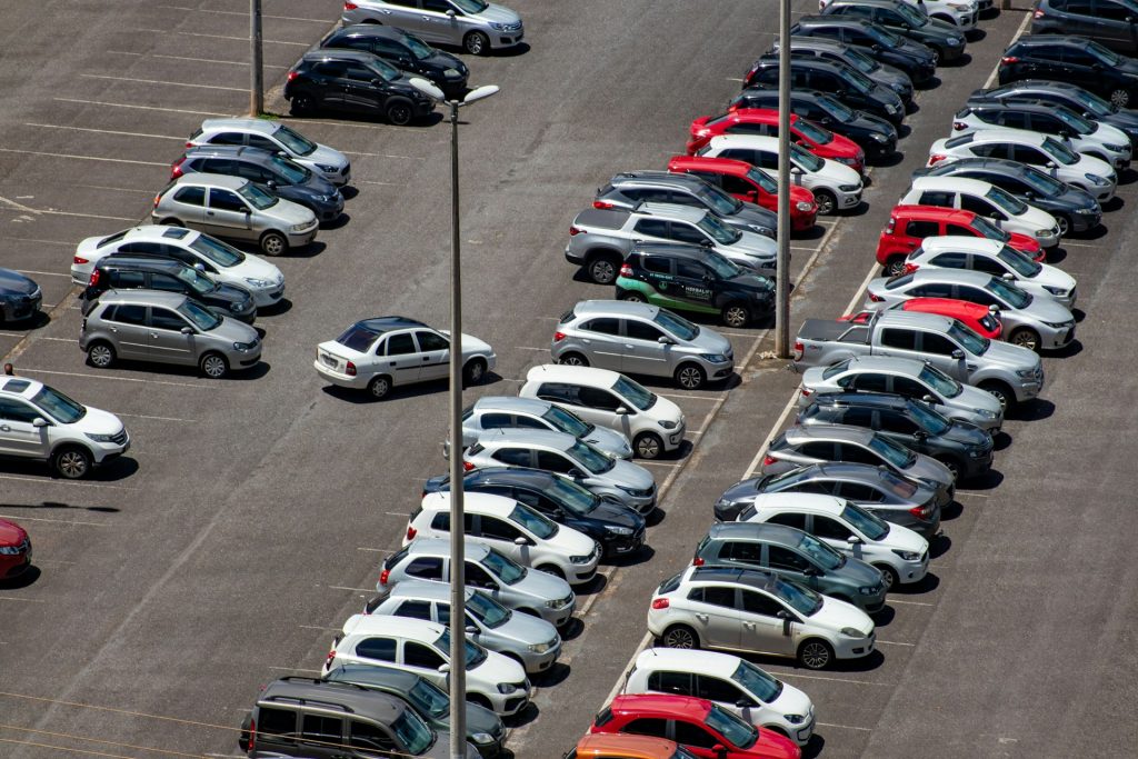 Aerial view of a large outdoor parking lot with rows of cars in the sun.