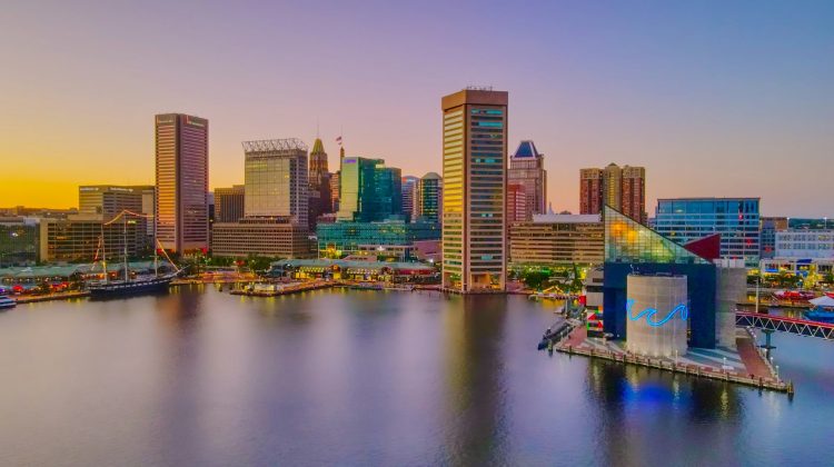 Baltimore's Inner Harbor skyline at sunset with the National Aquarium and city skyscrapers reflected in the water.