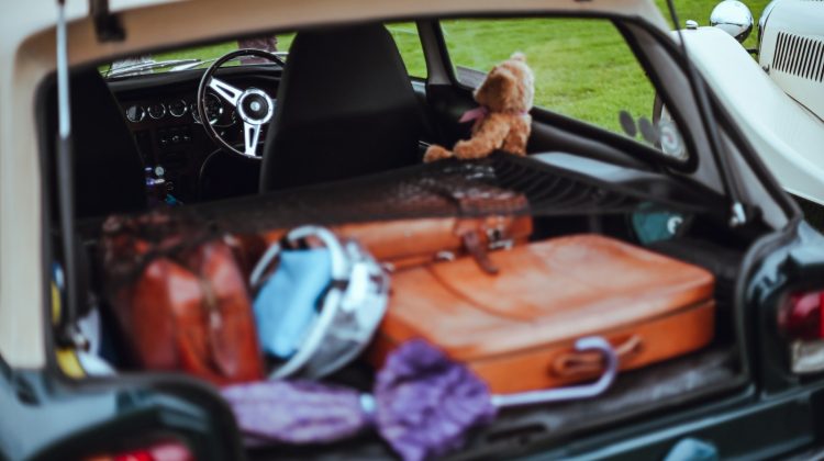 An open car trunk filled with suitcases, bags and a teddy bear ready for a move