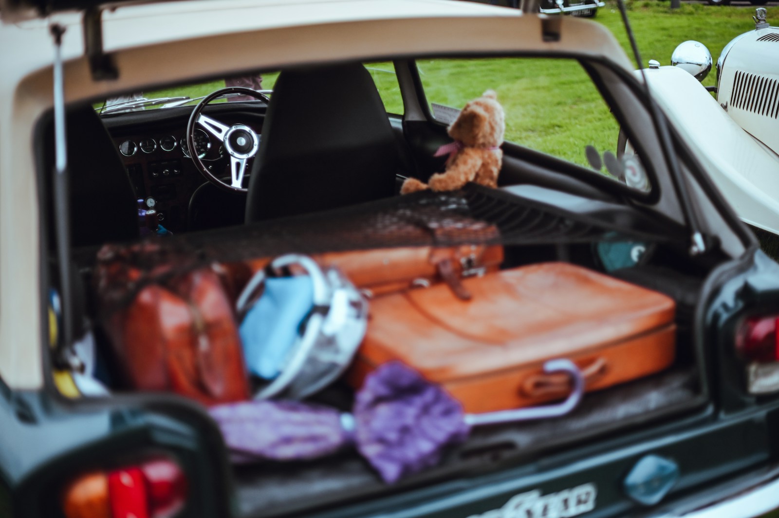 An open car trunk filled with suitcases, bags and a teddy bear ready for a move