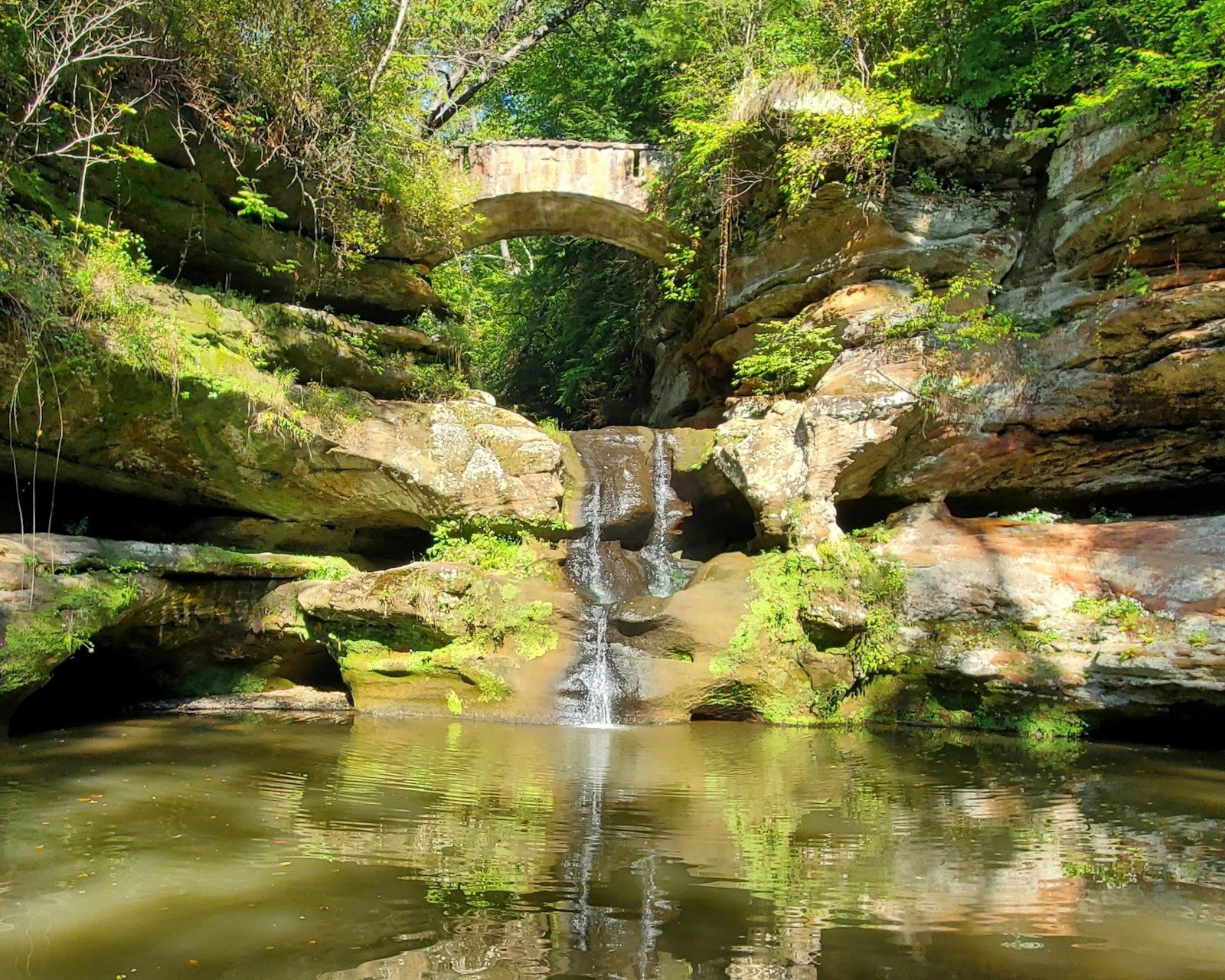 A waterfall flowing beneath a footbridge surrounded by forest at Hocking Hills State Park in Ohio