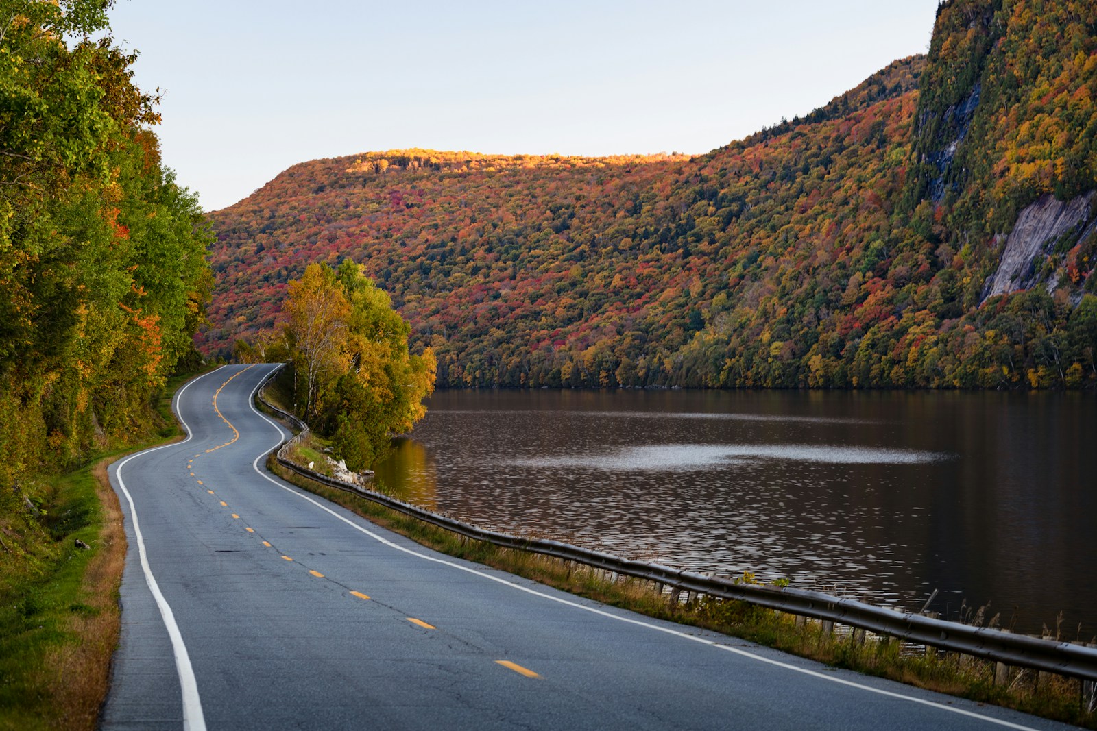 A winding road beside water surrounded by autumn trees in New England