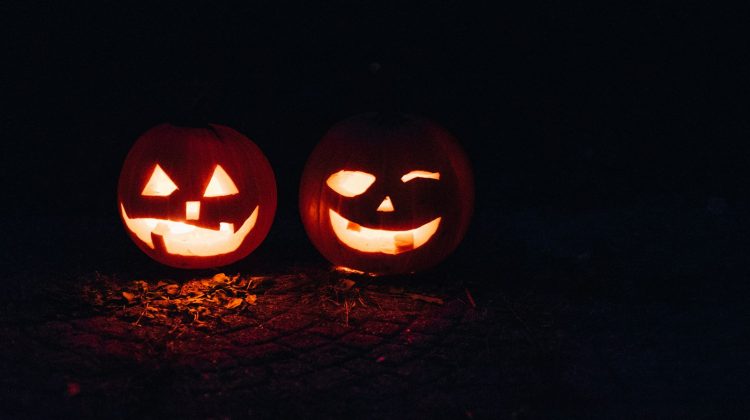 Two carved jack-o-lanterns glowing orange in the dark on a bed of leaves